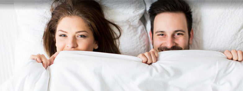 Girl and man lying in bed by holding the bedsheet together.