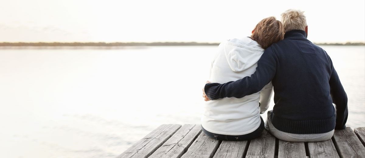 A couple hugging on a dock with beautiful sunset over a calm ocean.